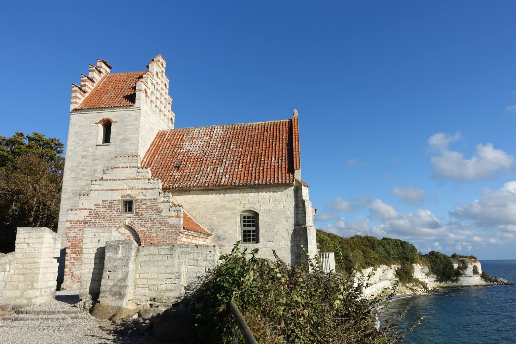 Kalkstenen kerkje met rood zadeldak op de rand van klif Stevns Klint