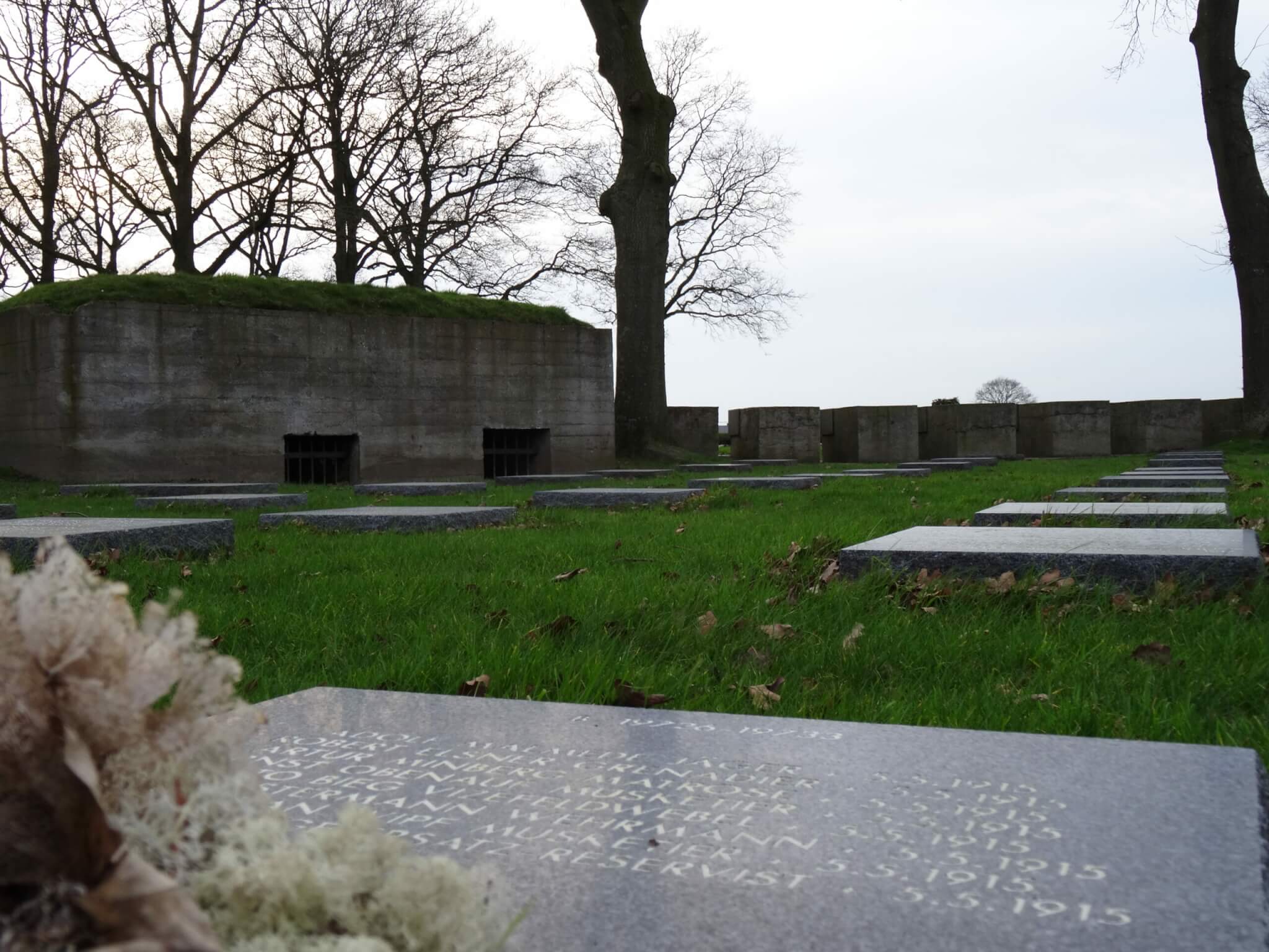 Platte grafstenen in het gras voor een betonnen bunker op Studentenfriedhof Langemark